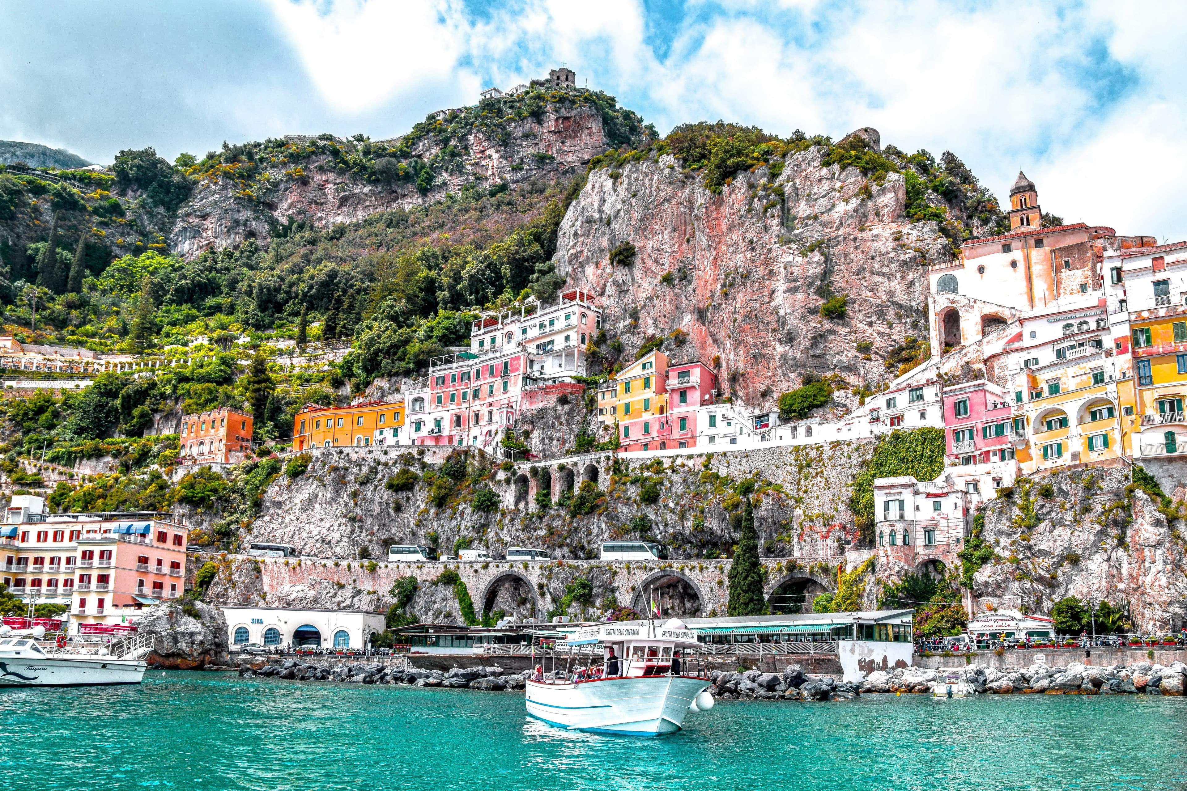 Pastel houses stacked down a cliff above turquoise water on the Amalfi Coast