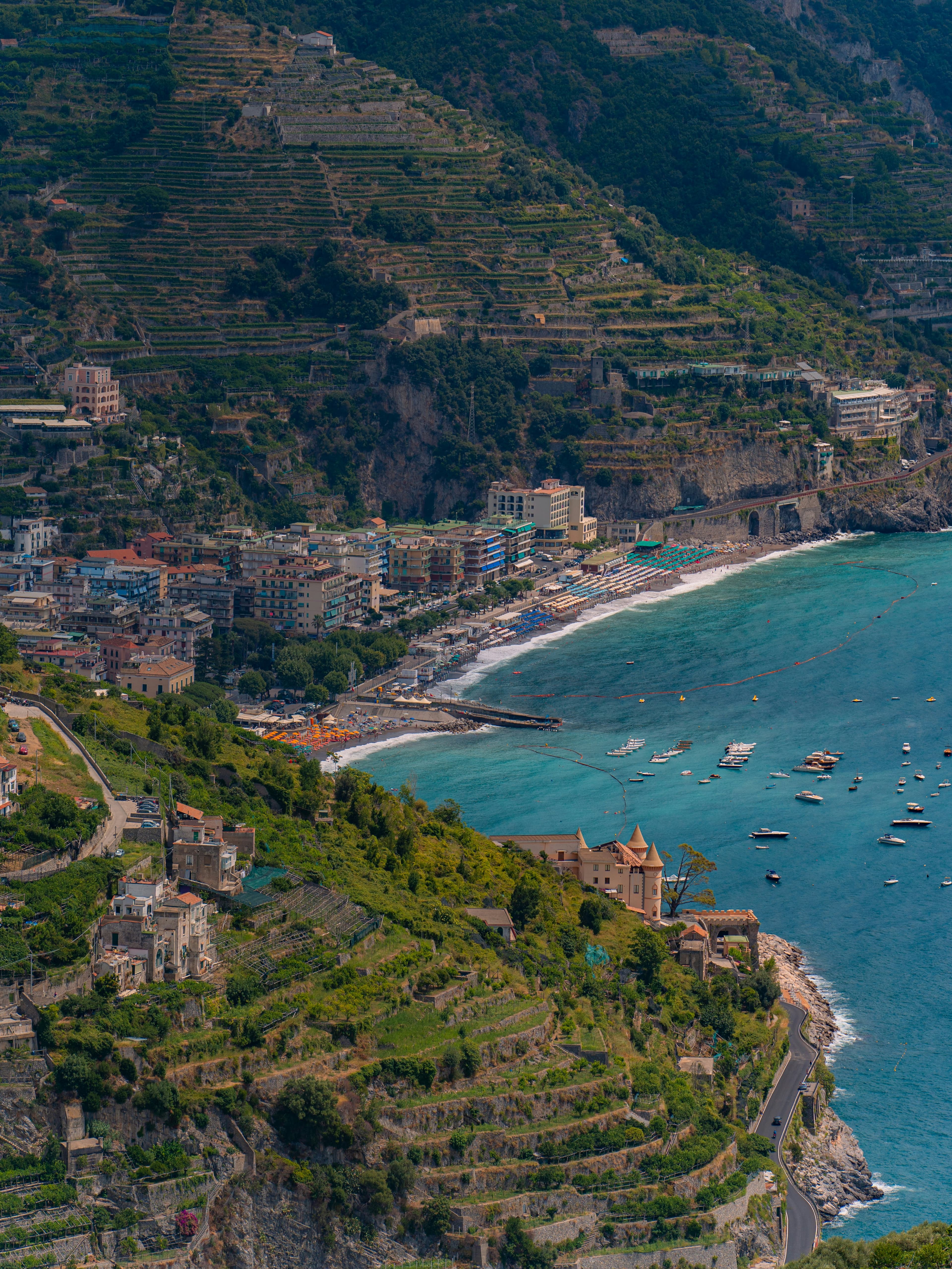A crescent bay of boats and beach umbrellas below a coastal town